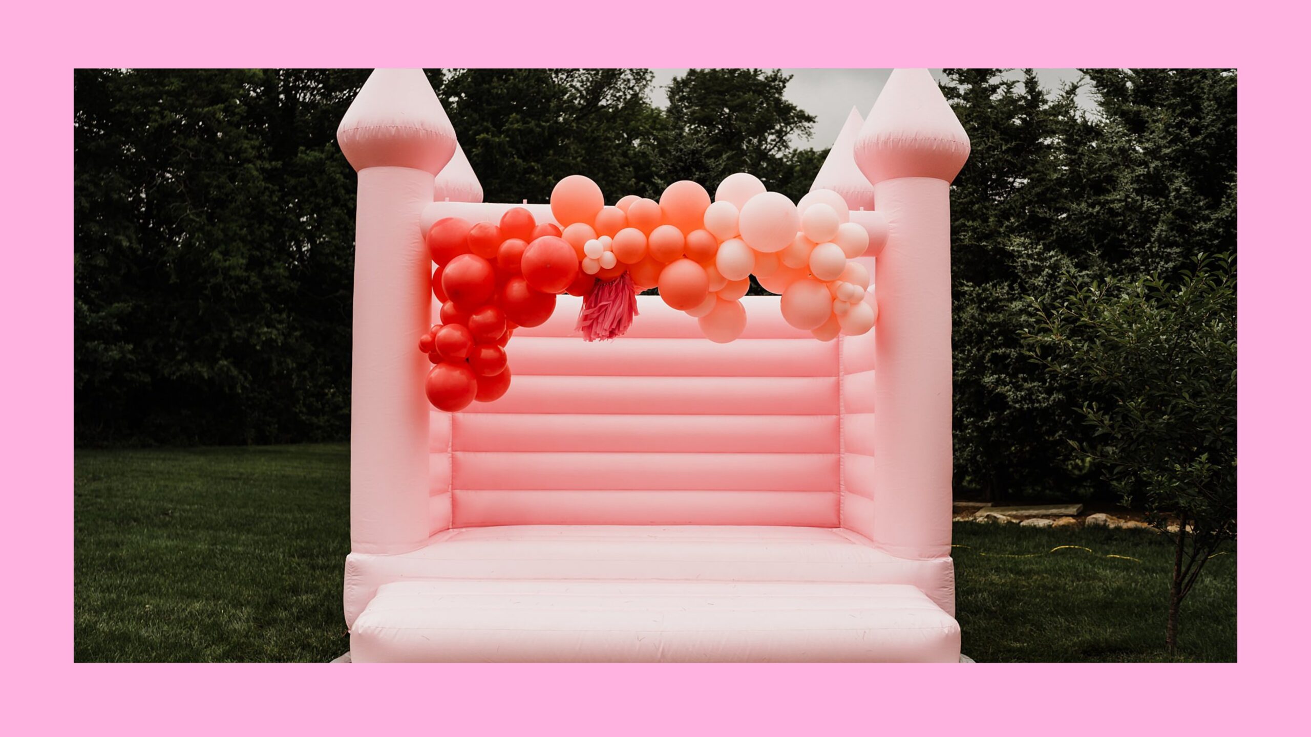 A pink bounce house with pink balloons on it.