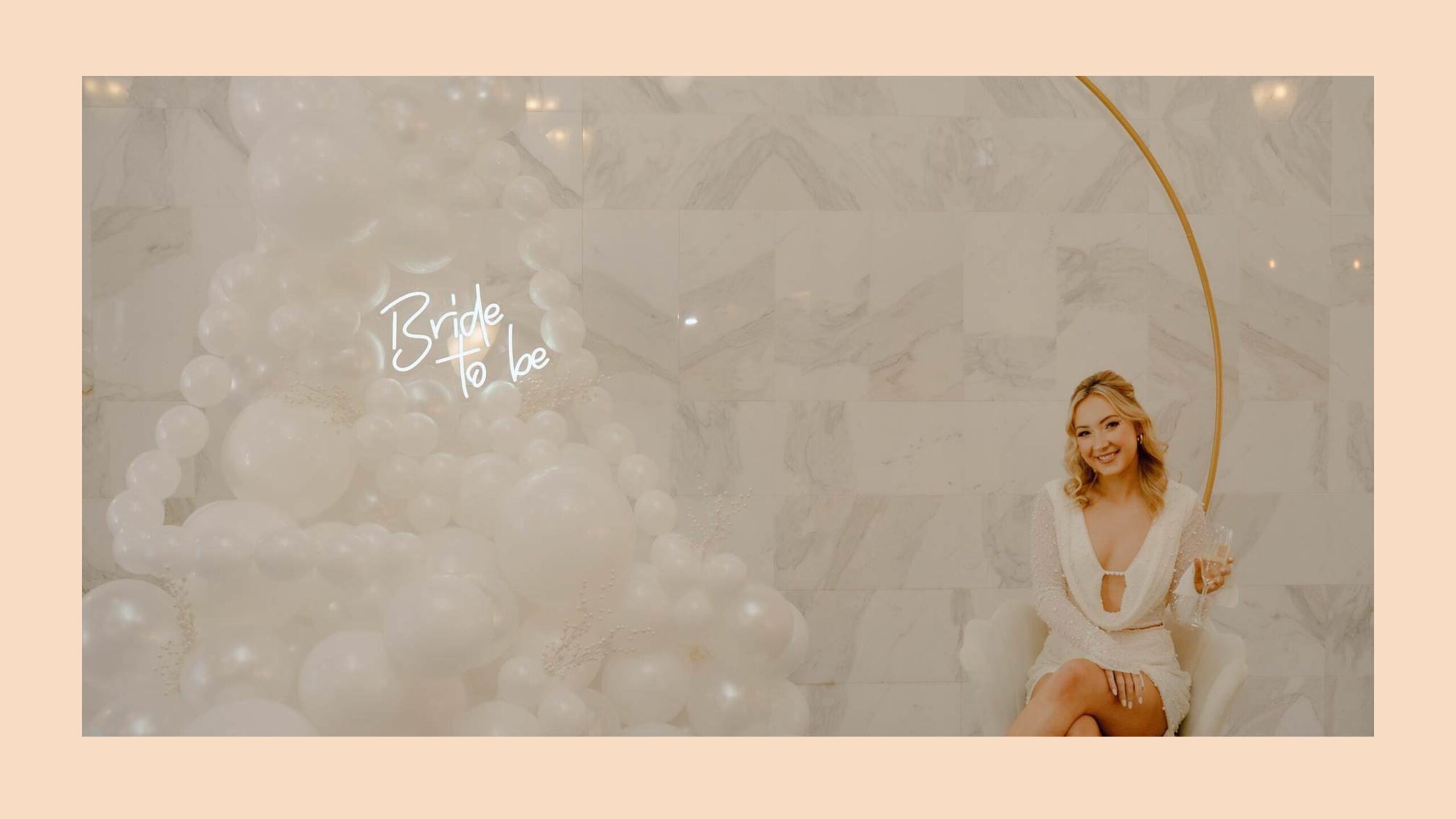 A woman in a short white dress, sitting in front of a white balloon arrangement.