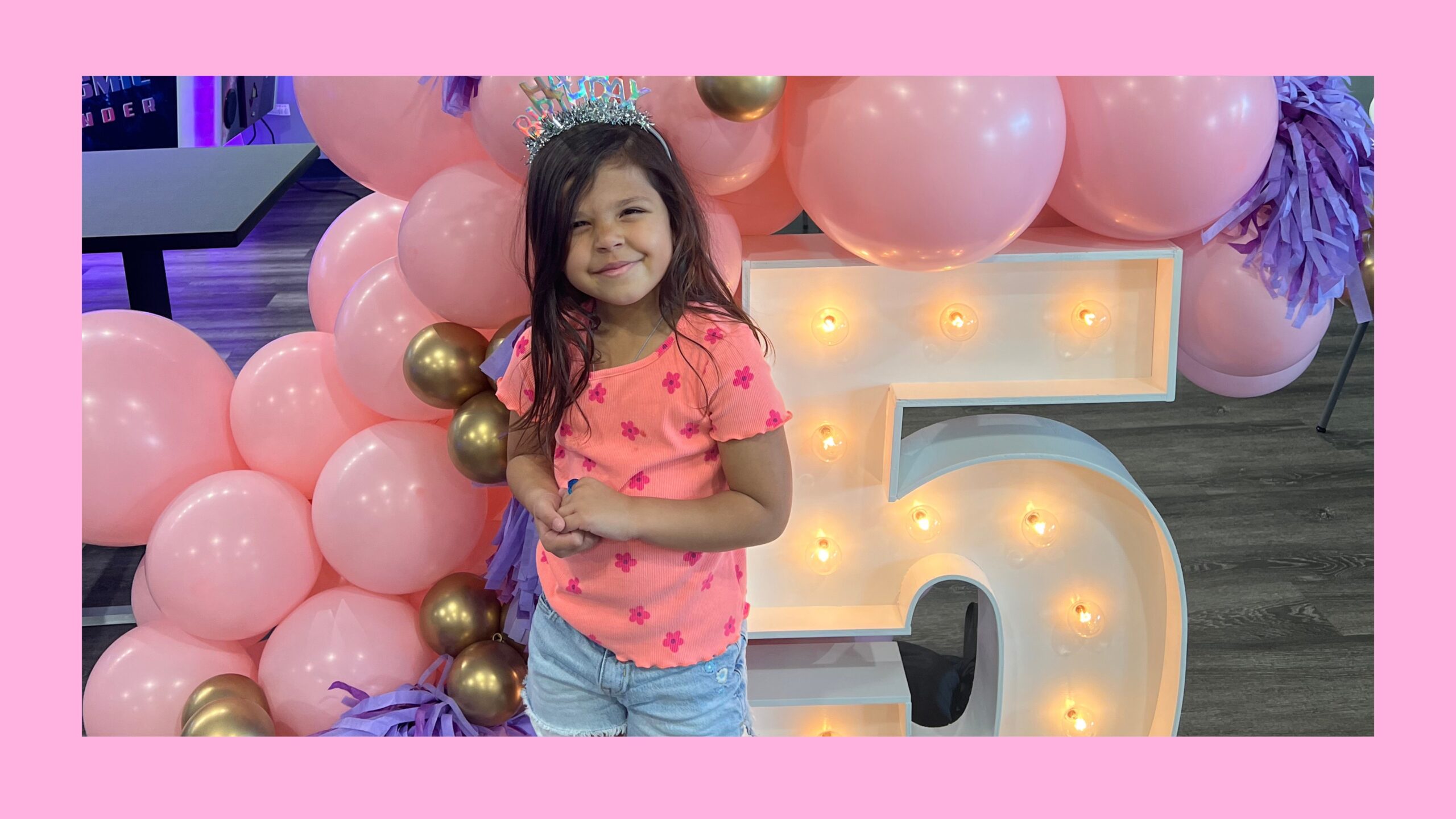 A little girl standing in front of pink balloons and a 5 marquee.