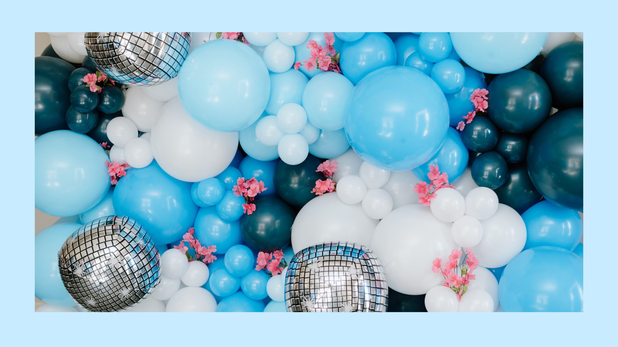 A blue, white, and navy balloon wall with pink flowers.