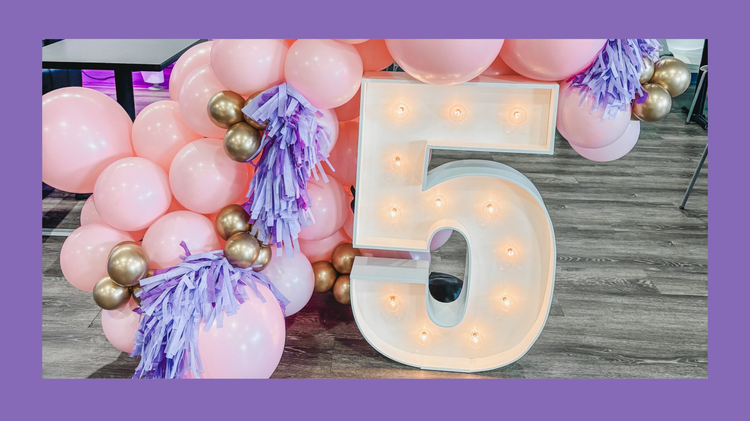 A 5 marquee surrounded by pink balloons and purple tassel fringe.