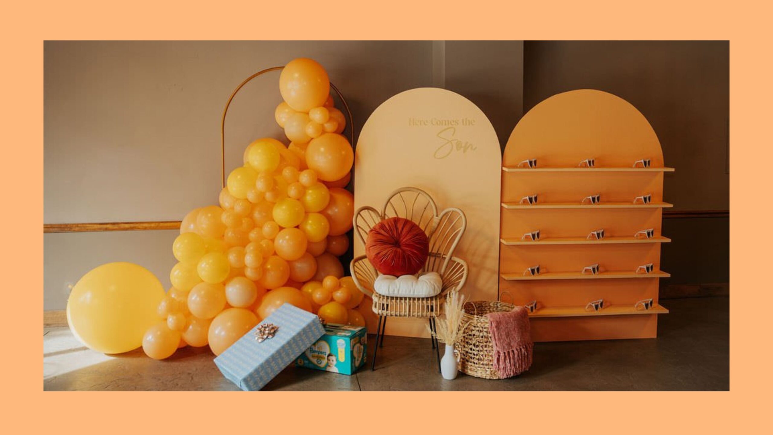 Orange balloons surrounding an orange backdrop with gifts sitting on the floor.