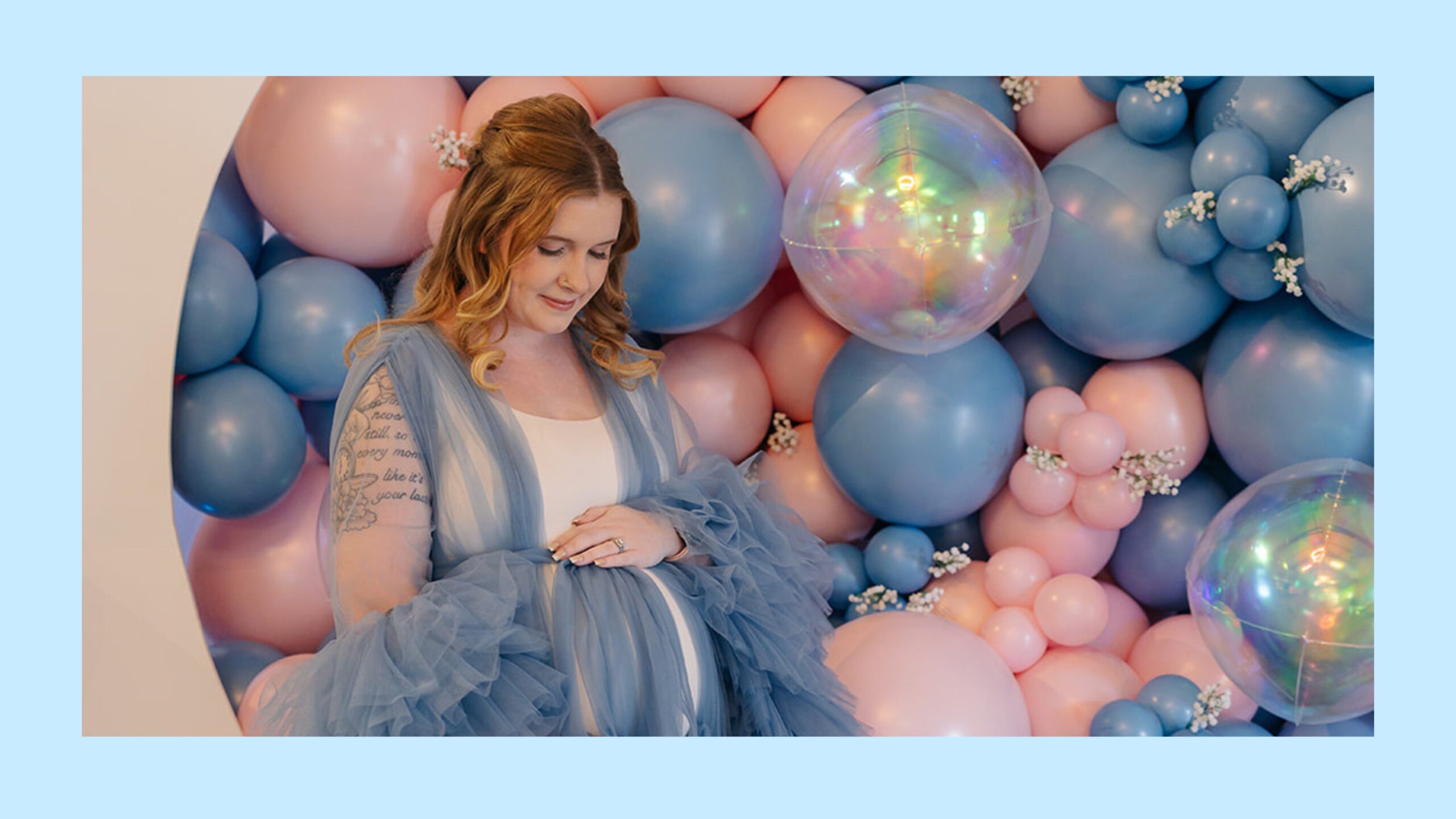 A pregnant woman stands in front of pink and blue balloons.