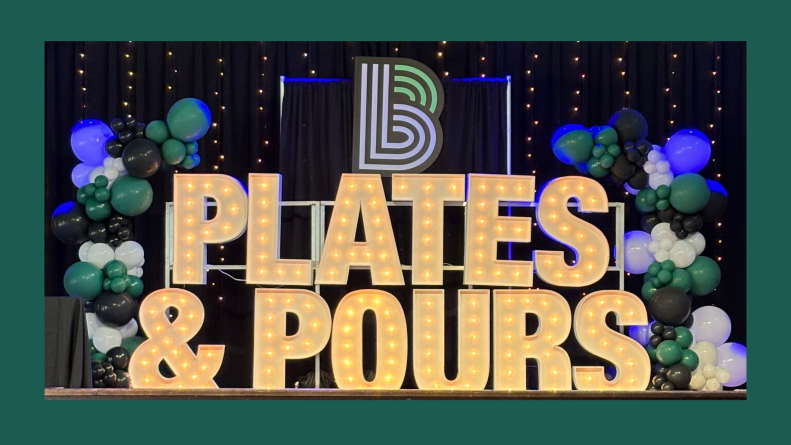 Plates & Pours spelled out in marquees sitting on a stage surrounded by green and white balloons.