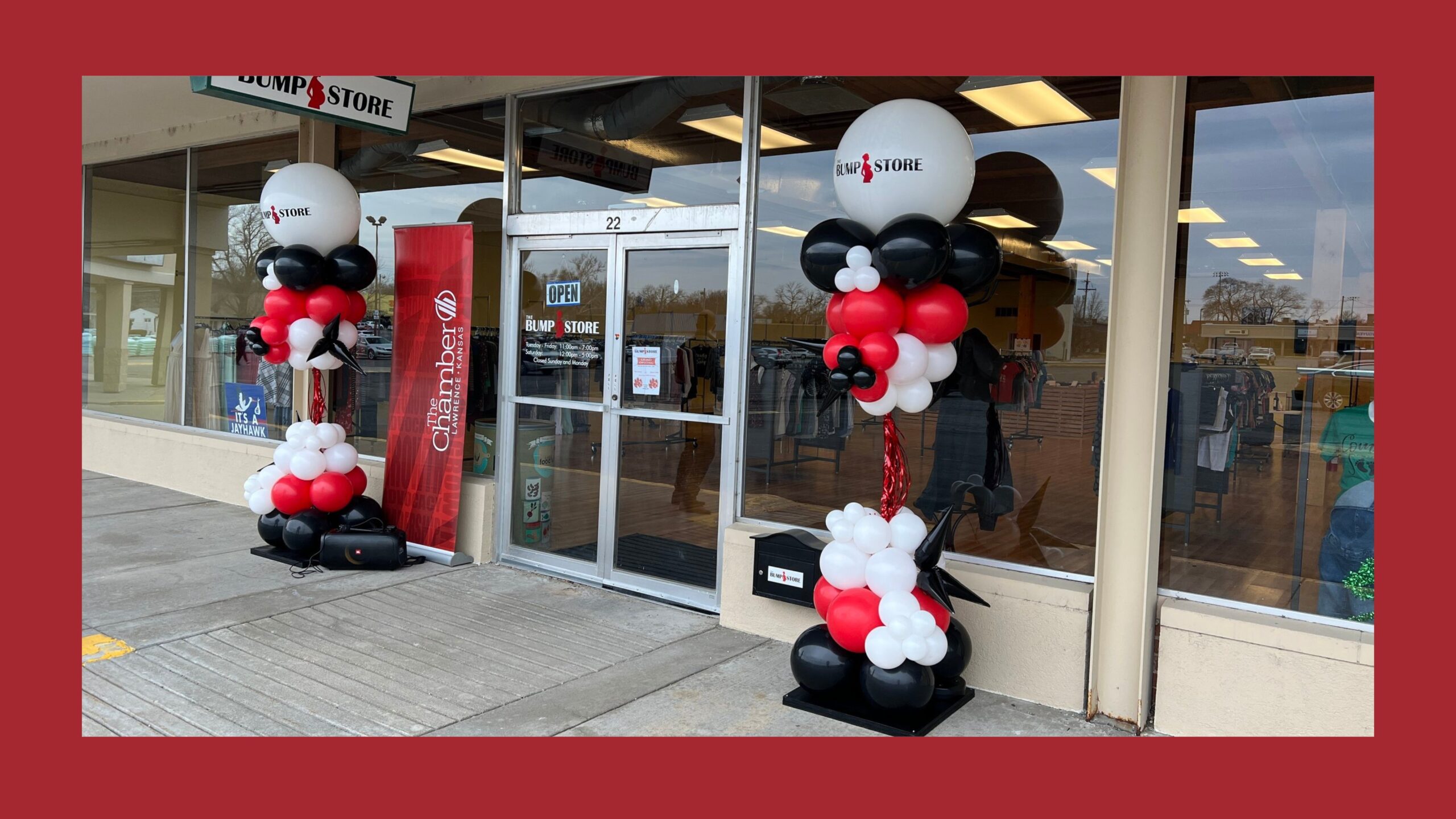 Two balloon columns sitting in front of a store front made up of white, black, and red balloons.