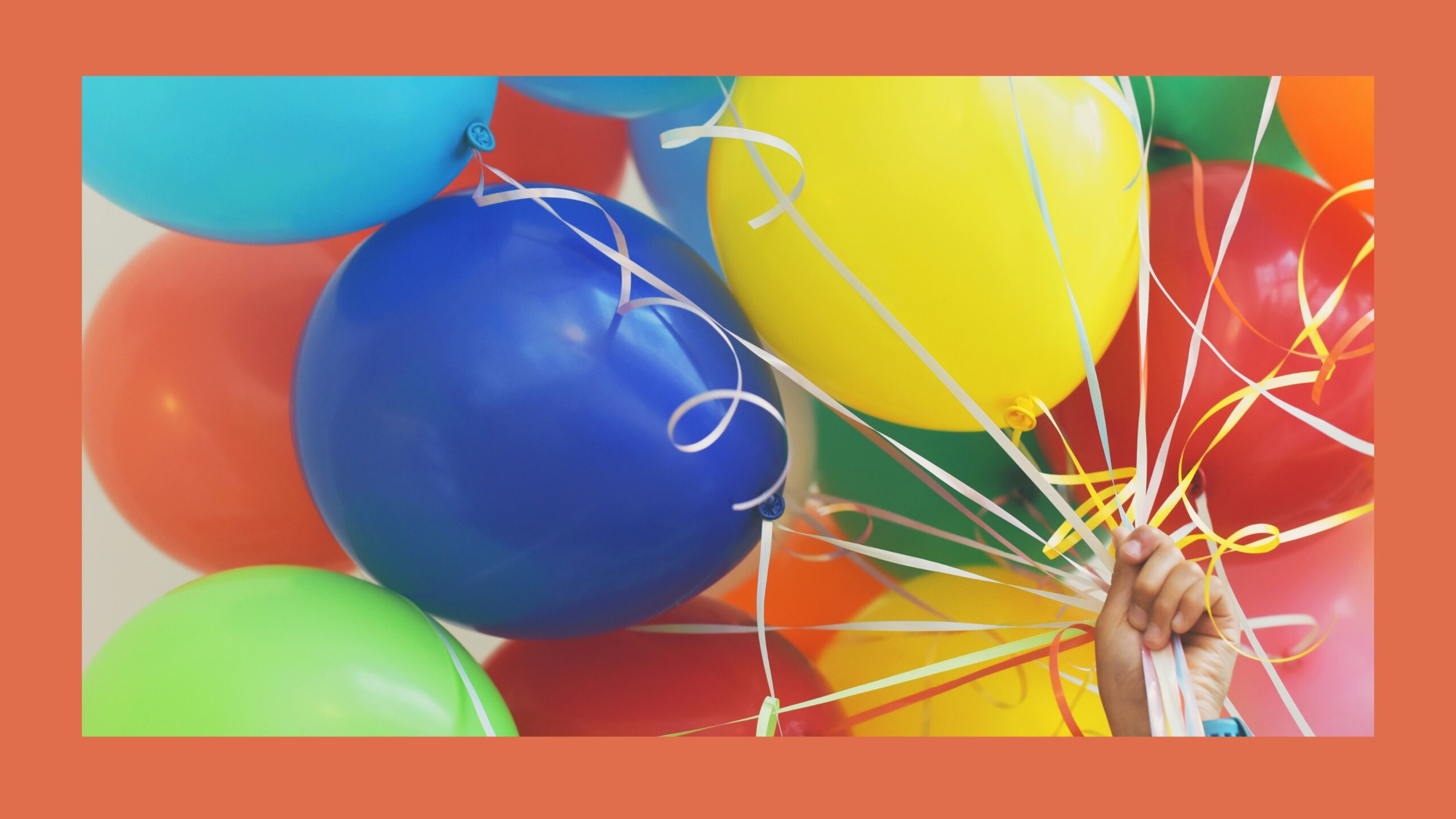 Colorful balloons filled with helium being held by a hand.
